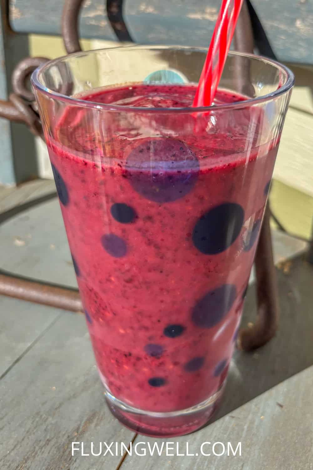 raspberry blueberry smoothie in a cup with a straw on a blue chair